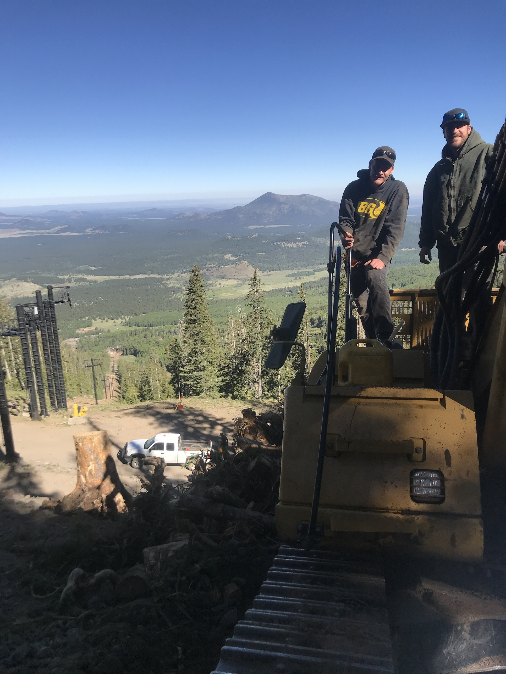 Two Mountainside Fleet mechanics standing on heavy equipment high on a mountain